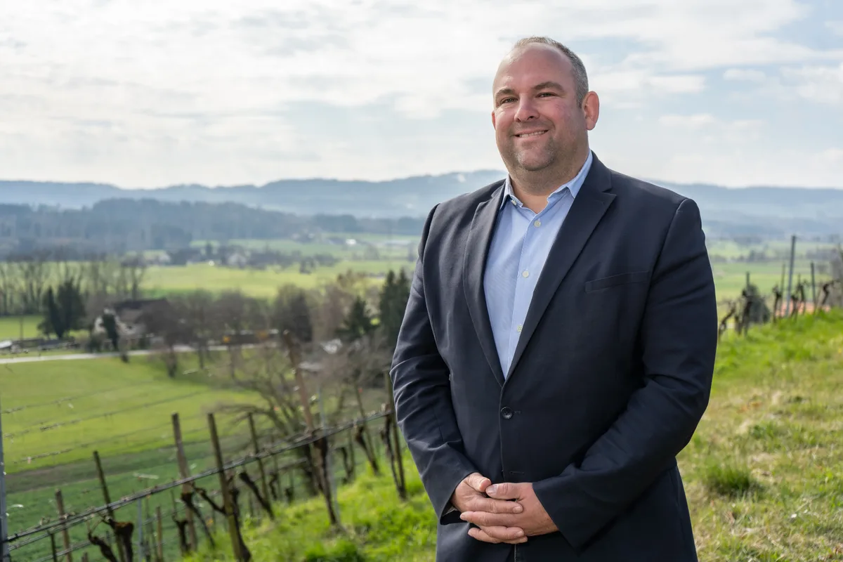 Ein Mann im Anzug steht vor einer Landschaft.
